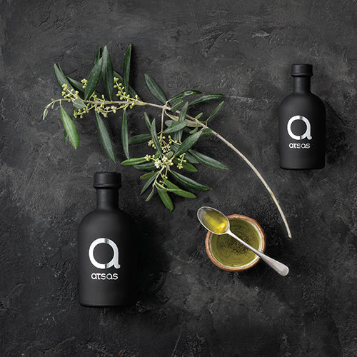 Premium black bottle of Atsas Silver high-polyphenol extra virgin olive oil with fresh olives and olive branch